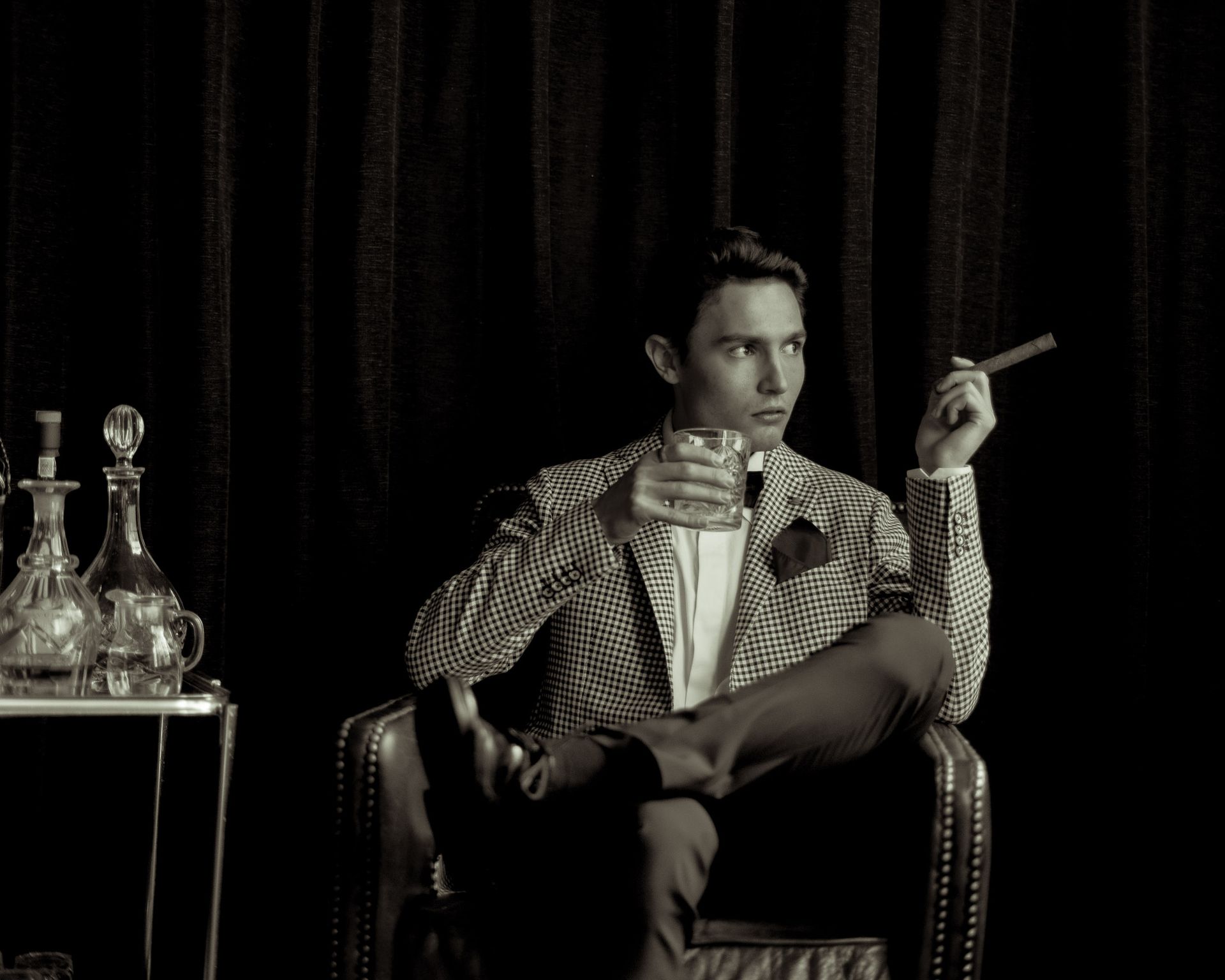 A man in formal attire relaxes with a cigar and whisky in a luxurious setting. Perfect for lifestyle or fashion themes.