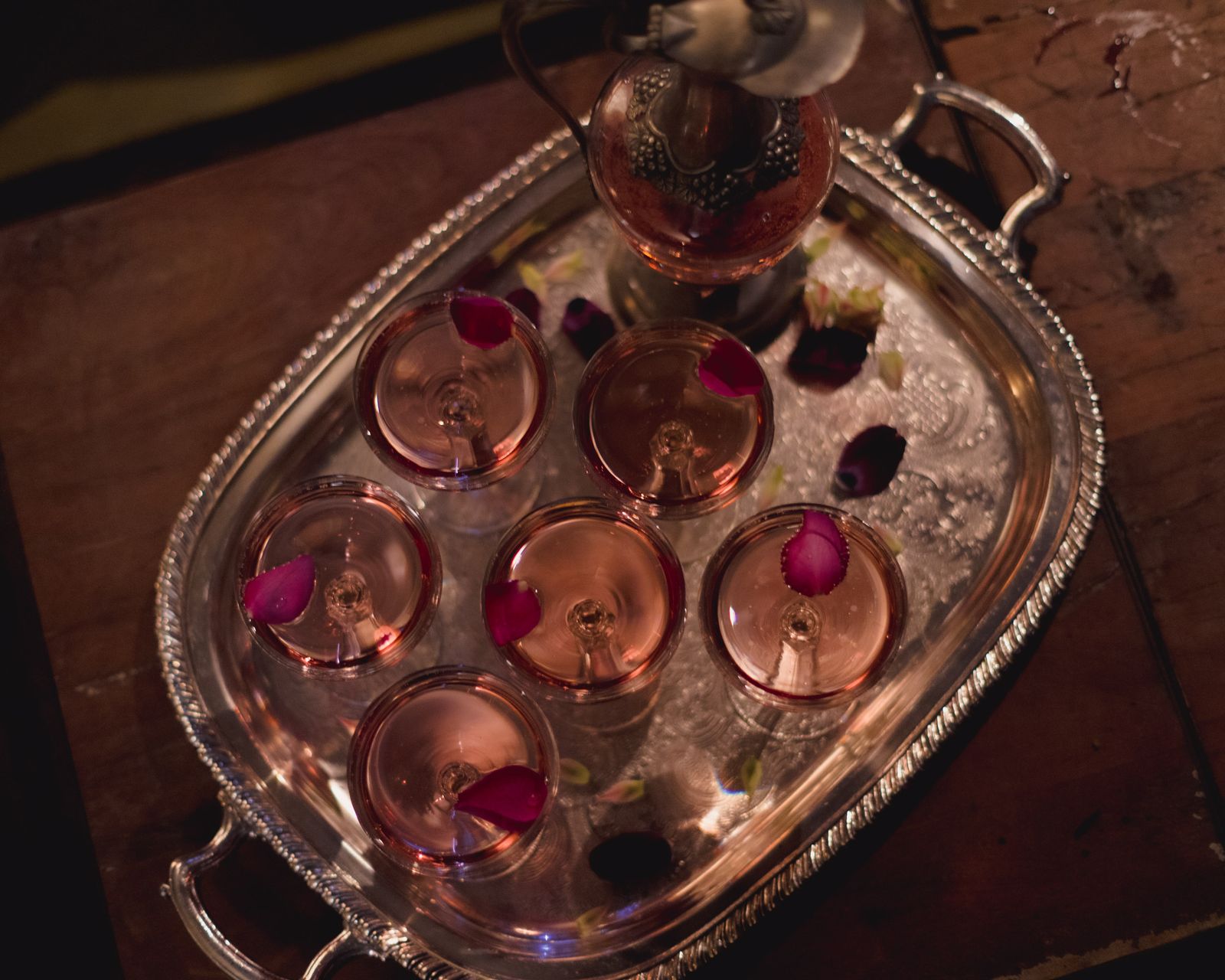 A silver tray of rose-tinted botanical spritz coupes on a dark bar top. Photo by Tanya Volt on Pexels