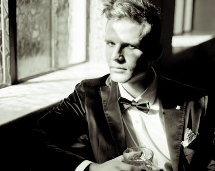 Classic black and white portrait of a man in formal attire holding a glass, exuding elegance.