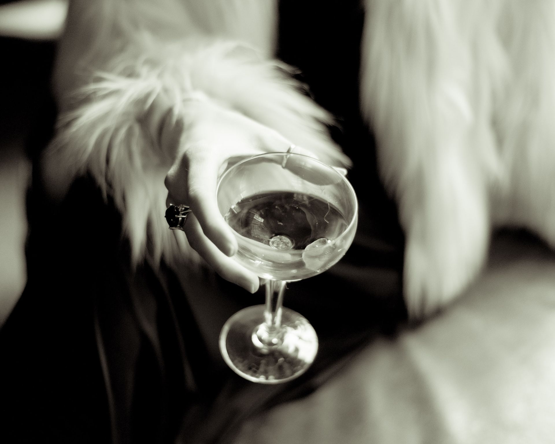 Close-up of a woman's hand holding a cocktail glass with a fur coat, exuding elegance and luxury.