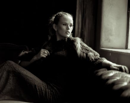 Sophisticated woman in fur and lace dress posing in a luxurious, low-light setting.