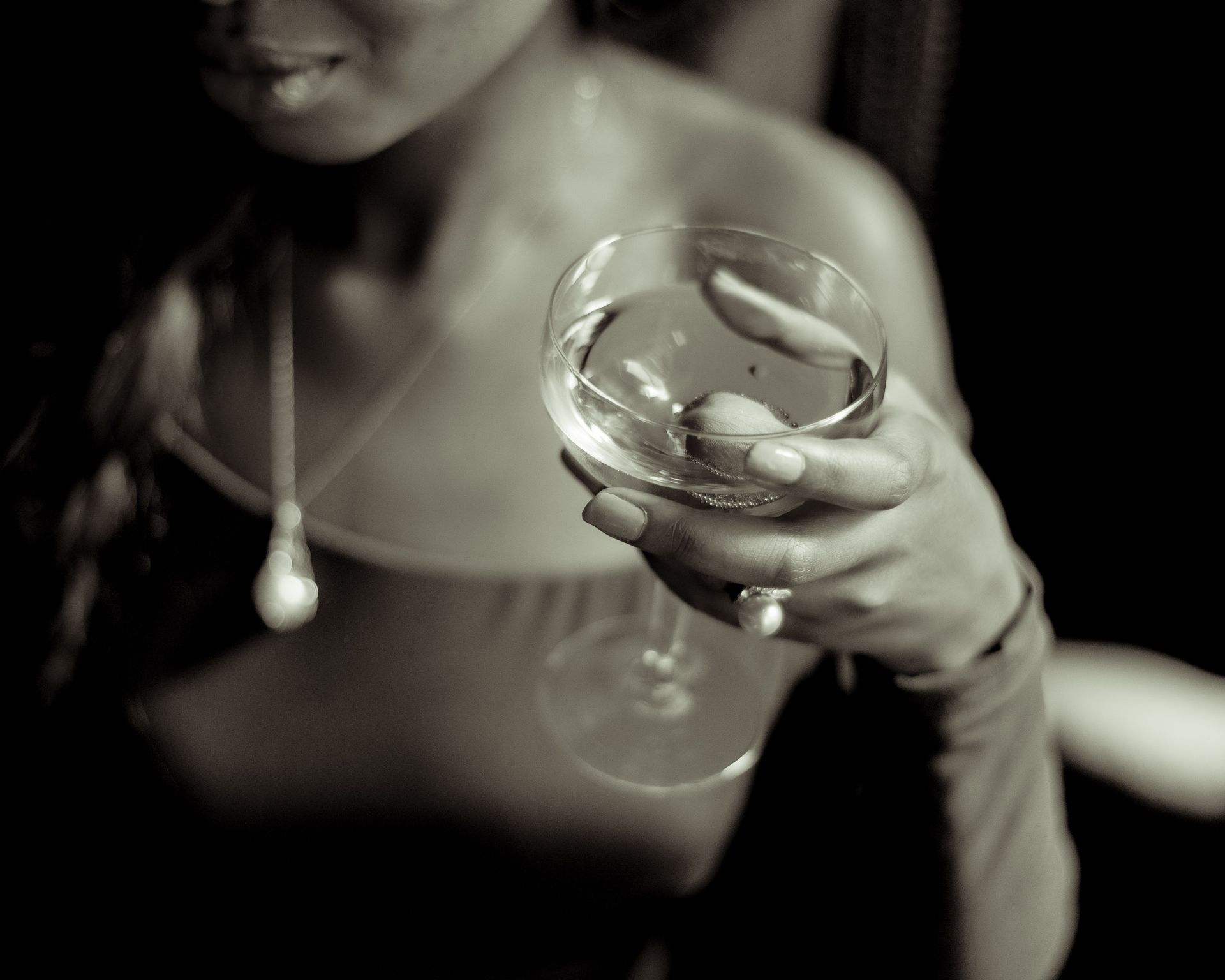 A stylish woman elegantly holding a cocktail glass in a dimly lit setting.