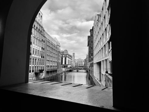 Free Monochrome cityscape featuring river, buildings and cloudy sky through an archway. Stock Photo