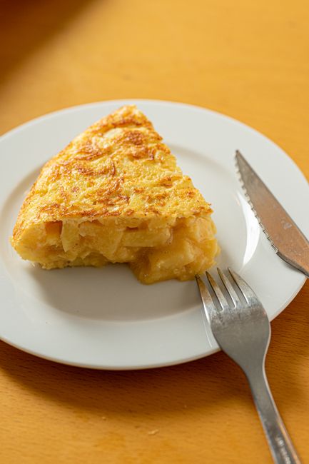 A delicious slice of Spanish tortilla with a fork and knife on a white plate.