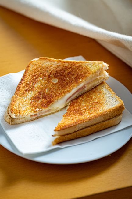 A grilled cheese sandwich cut diagonally on a plate, showing melted cheese stretching between the two halves and a deep golden-brown crust.