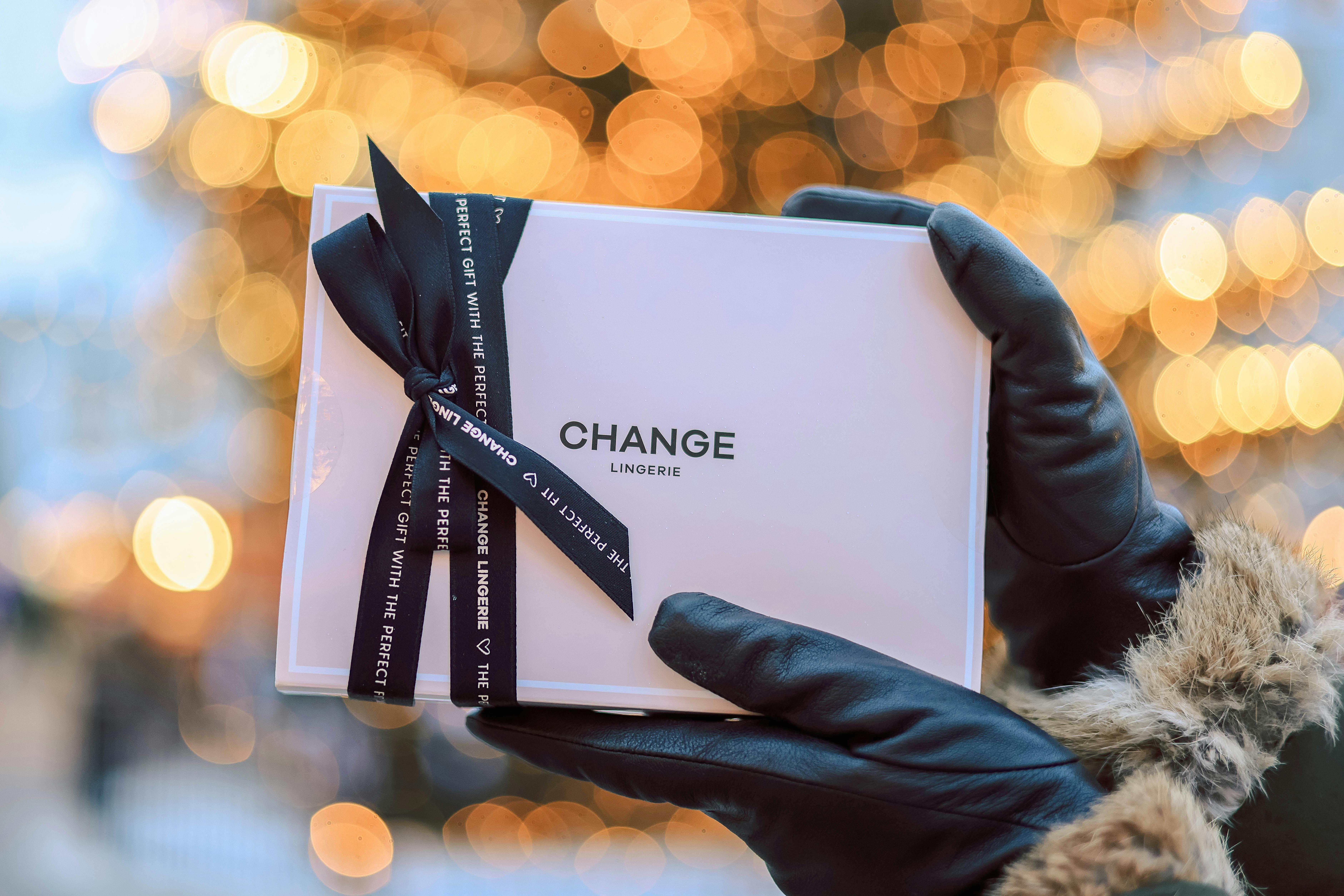 Close-up of a gift box with ribbon held by gloved hands. Festive bokeh background.