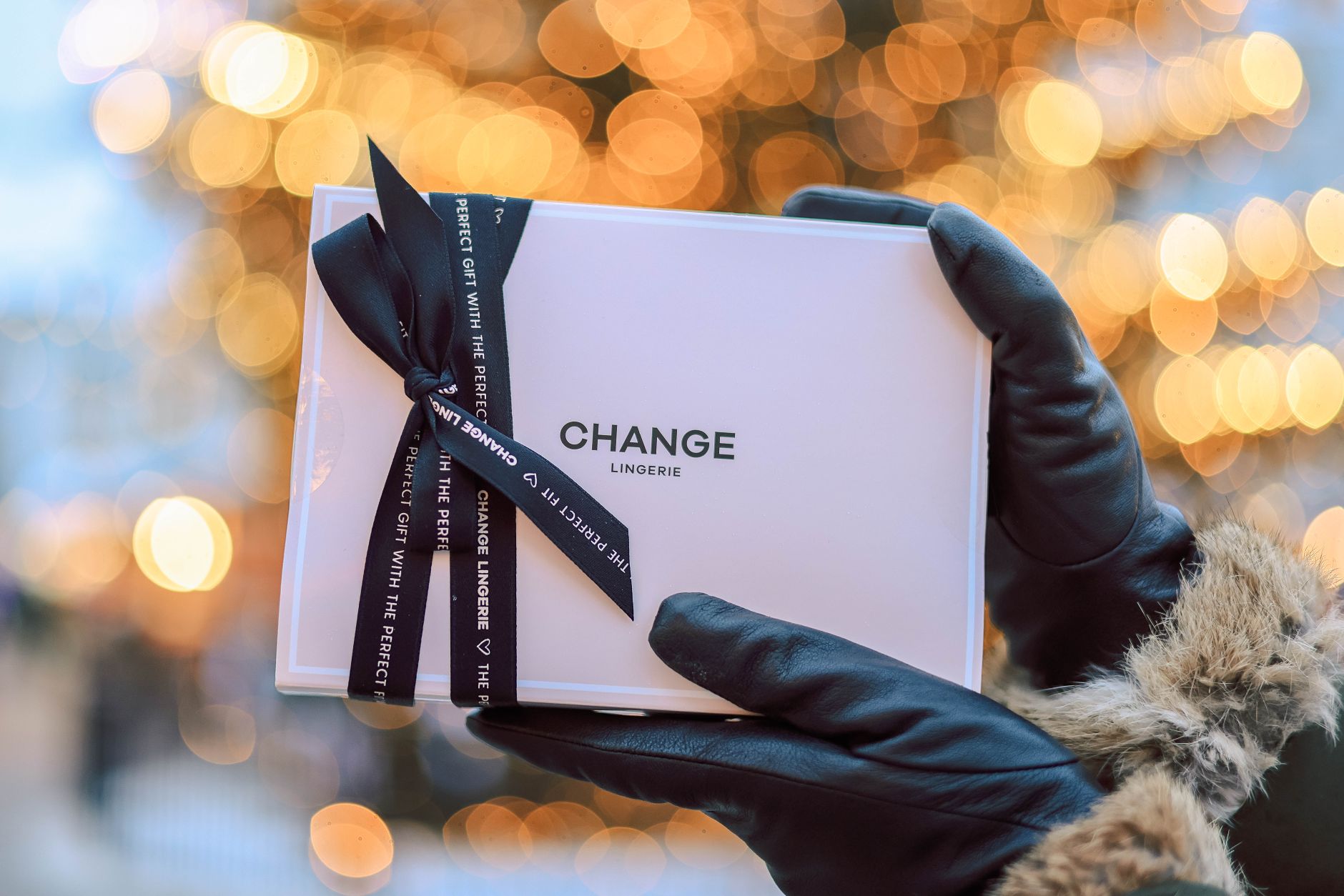 Close-up of a gift box with ribbon held by gloved hands. Festive bokeh background.