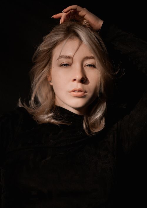 Free Striking portrait of a blonde woman fixing her hair, with dramatic lighting. Stock Photo