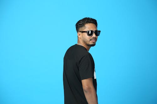Studio Shot of a Young Man in Sunglasses Standing against Blue Background