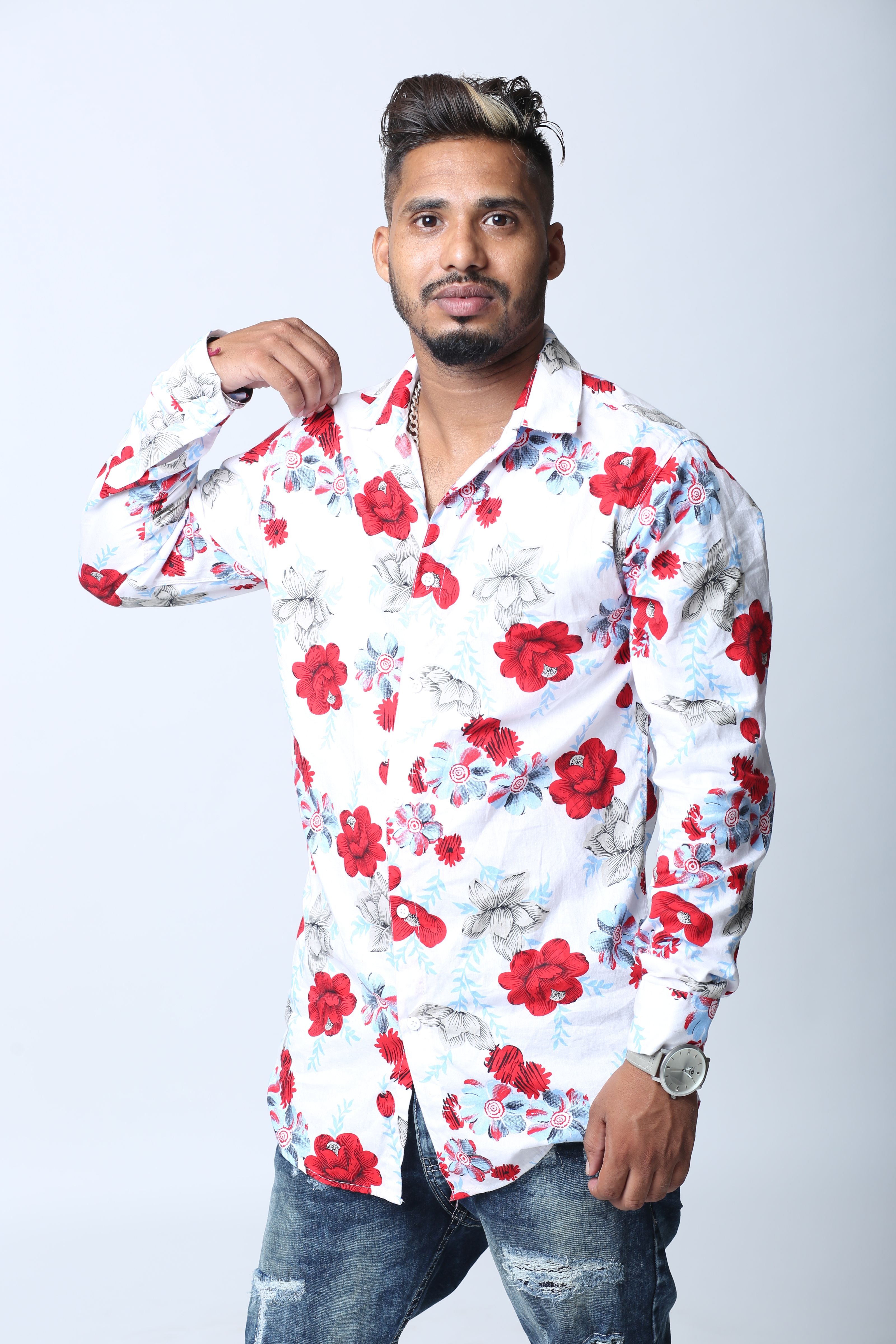 Homem vestindo uma camisa floral vibrante posa em um estúdio, exibindo um estilo de moda casual.