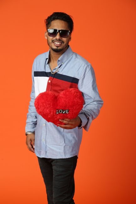 A stylish man poses with a red heart-shaped pillow in a studio setting, radiating happiness.