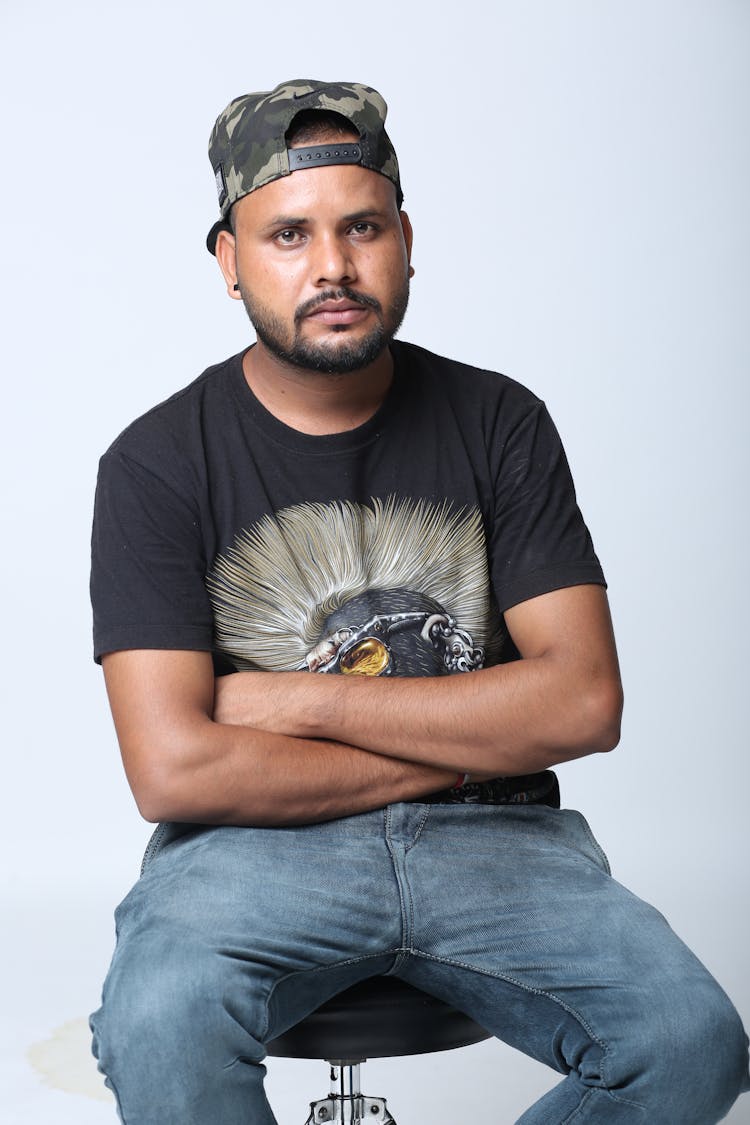 A Man In Black Shirt And Cap Sitting On A Stool