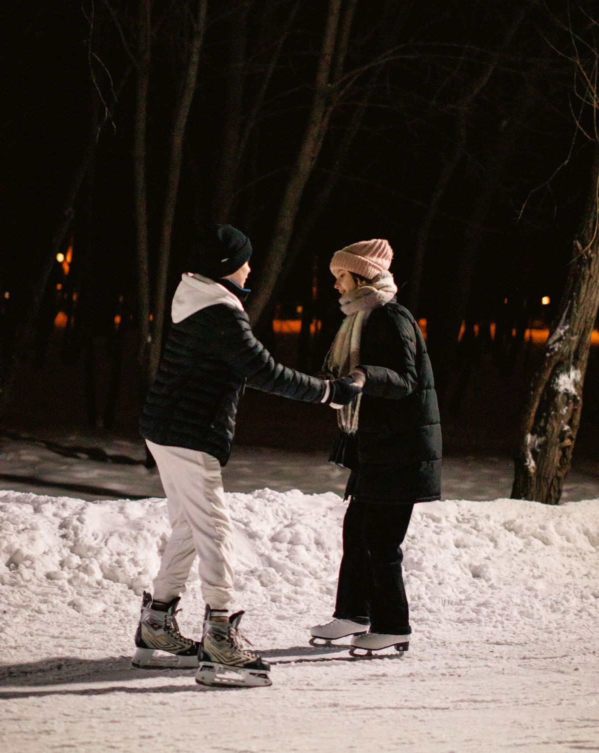 Couple ice skating together at night on an outdoor rink lit by string lights
