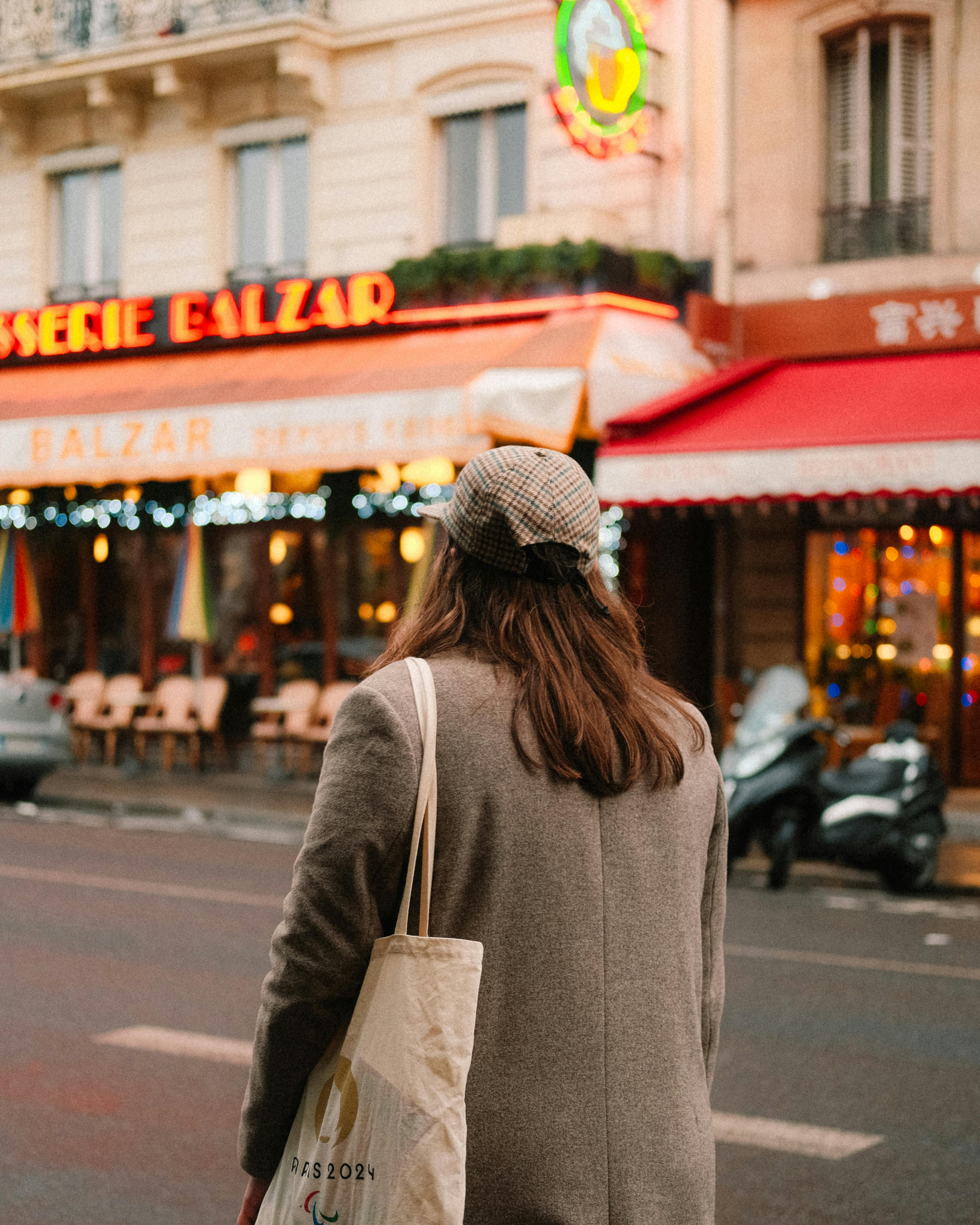 A woman with a tote stands before a Parisian café, capturing urban charm.