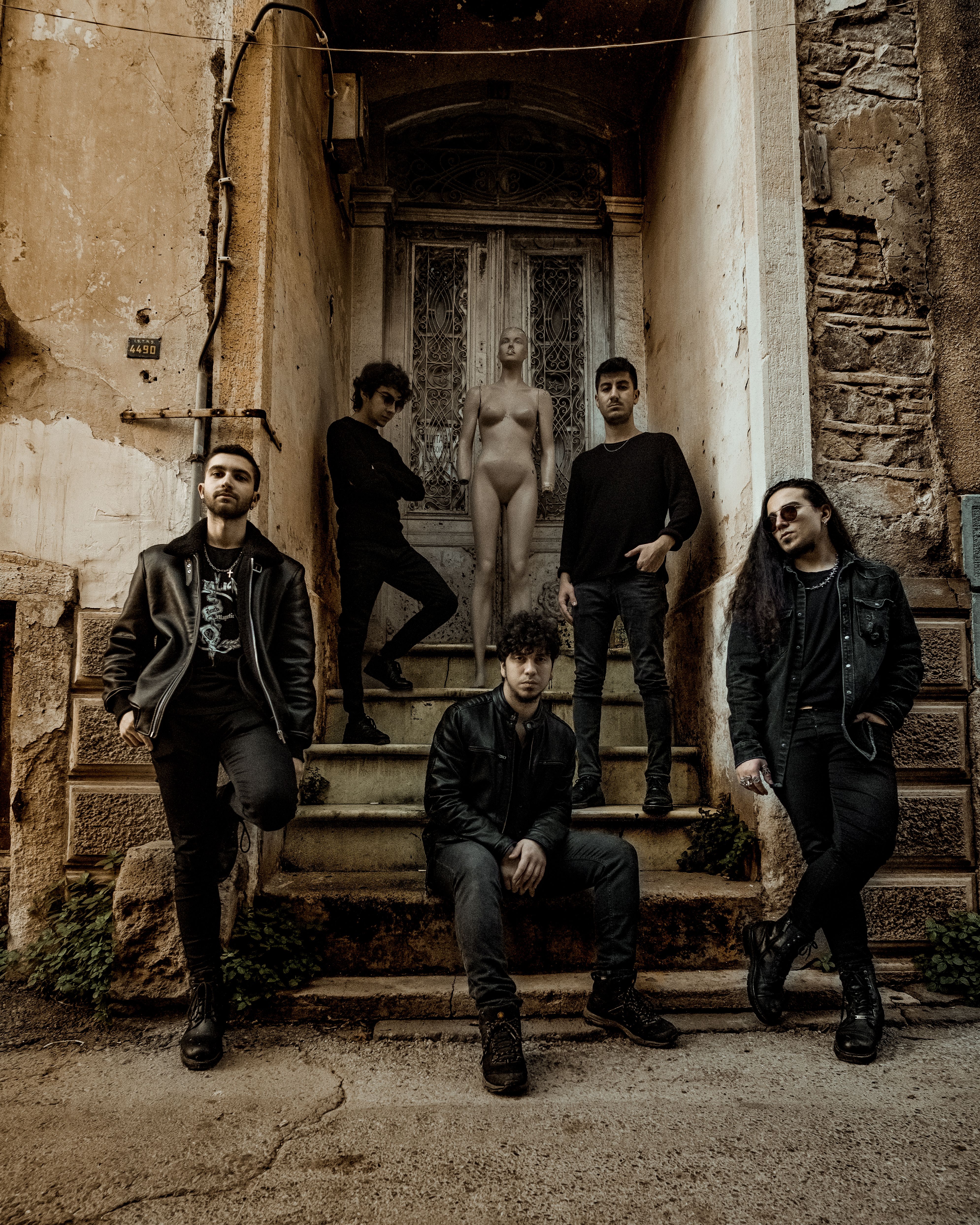 Five men posing with a mannequin outside an abandoned building, showcasing urban style and mystery.