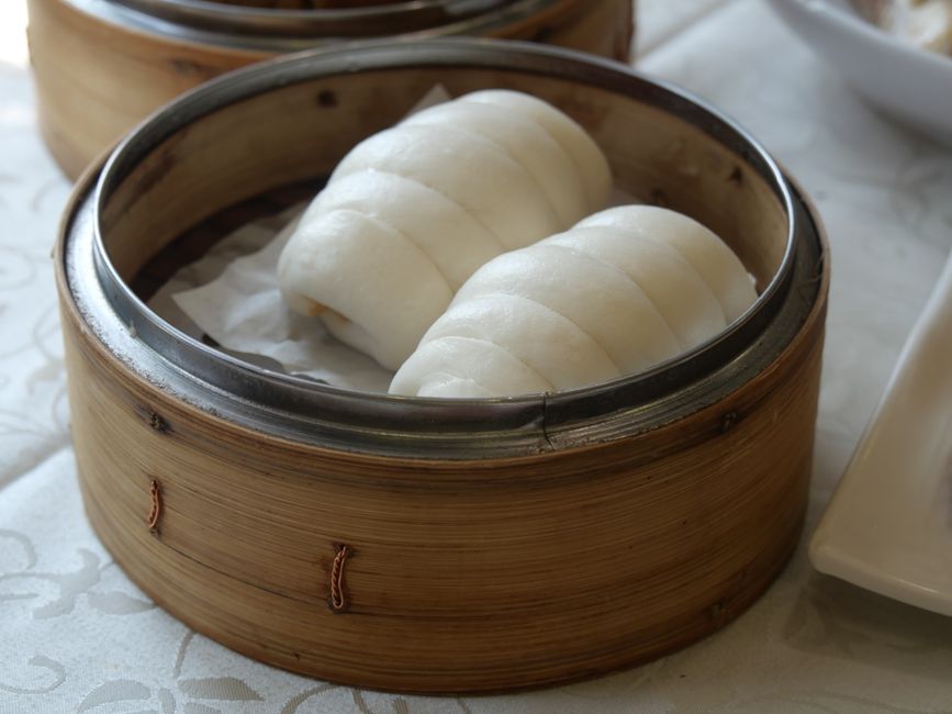 Two steamed bao buns in an open bamboo steamer basket`
