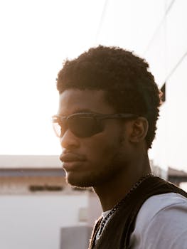 Portrait of a stylish Black man wearing sunglasses with sunlight in the background, taken outdoors in Nigeria.