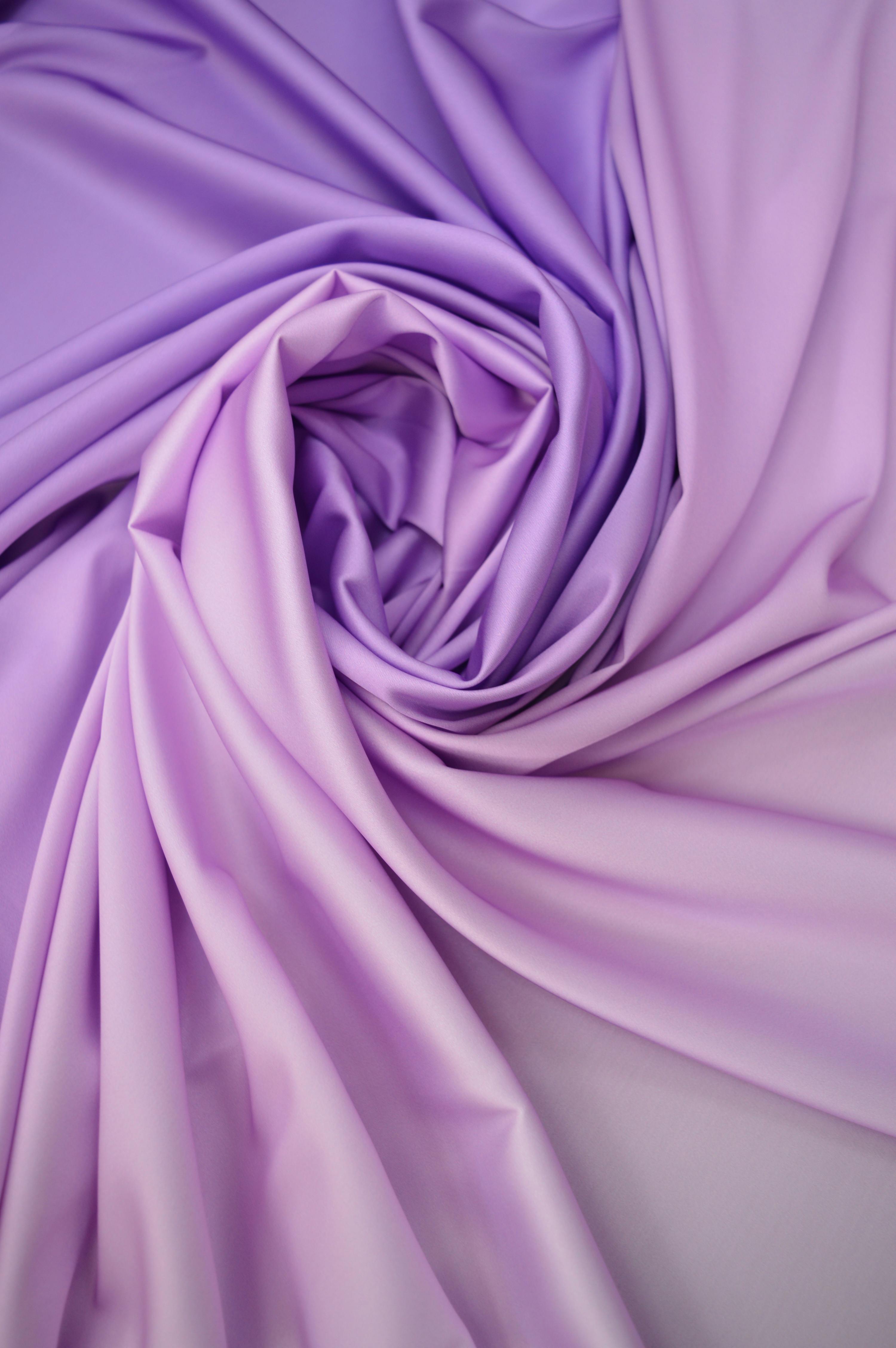 Close-up of draped lilac satin fabric forming an elegant swirl pattern, perfect for design and textile projects.