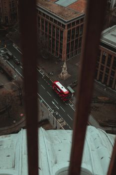 Aerial view of a red double-decker bus on a city street near a bus stop, framed by architectural structures.