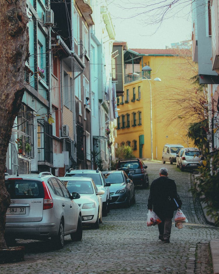 Man Carrying Shopping Bags Uphill Cobblestone Street