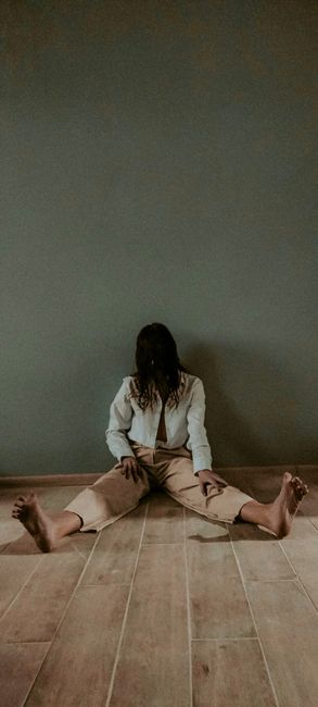 Fotomural Una persona está sentada descalza en un suelo de madera contra una pared desnuda, creando una atmósfera sombría.