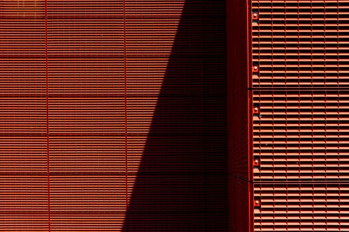 Free A modern red building facade with a dramatic shadow casting geometric patterns, creating an artistic urban visual. Stock Photo