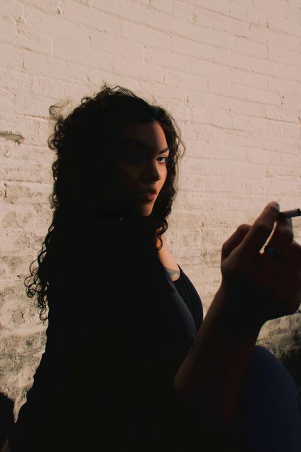 Moody silhouette of a woman smoking in front of a brick wall, emphasizing shadows and mystery.