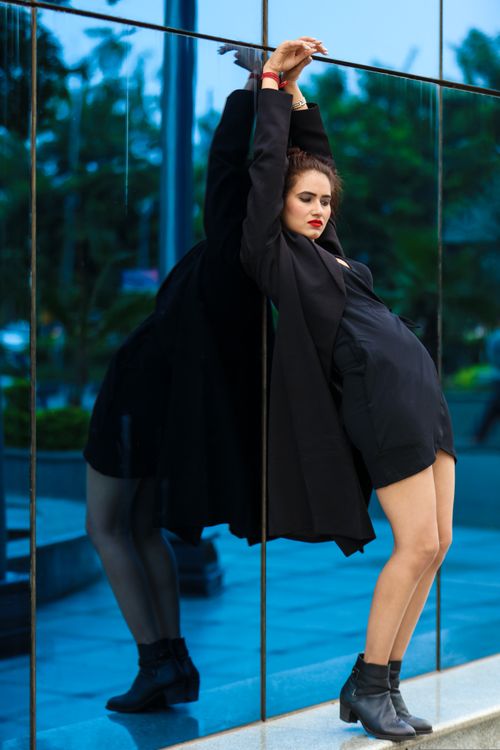Free Stylish woman in black ensemble poses against a glass wall with a striking reflection. Stock Photo