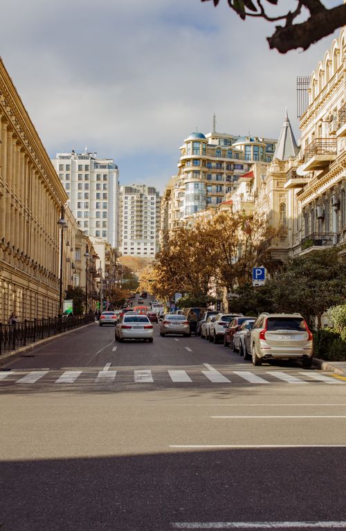 Free City street scene with cars, buildings, and crosswalk under a bright sky. Stock Photo