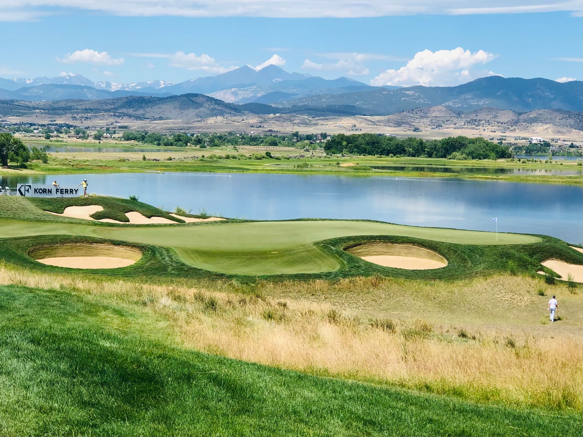 A scenic golf course near a tranquil lake with mountain views under a clear blue sky.