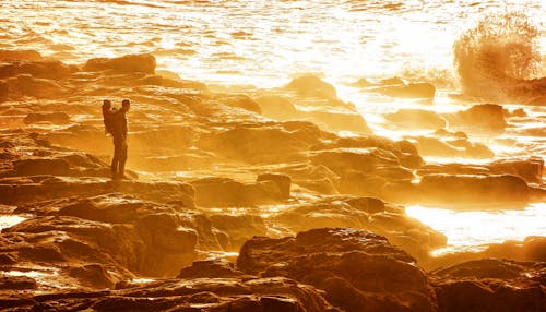 Free Man Standing on Rocky Shore during Sunset Stock Photo