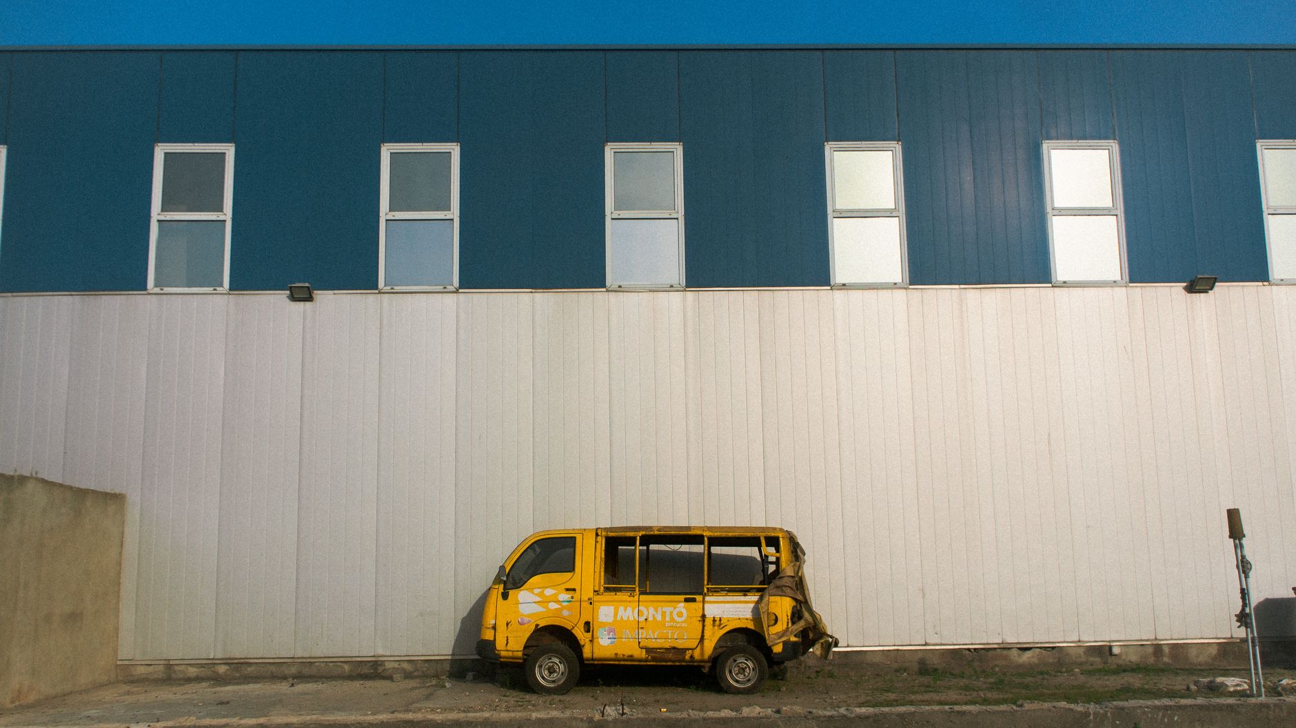 A dilapidated yellow danfo bus parked against a warehouse wall in Lagos, Nigeria.