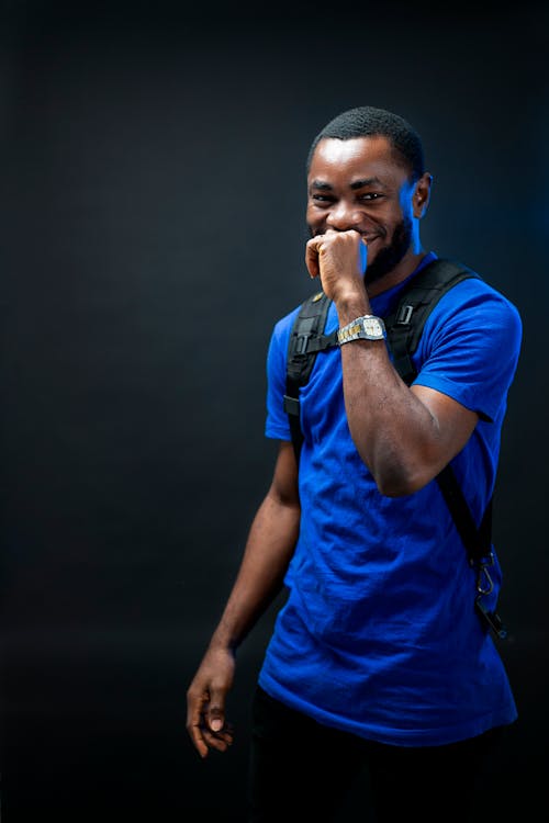 Studio Shot of a Young Man in a Blue T-shirt, Wearing a Backpack and Smiling 