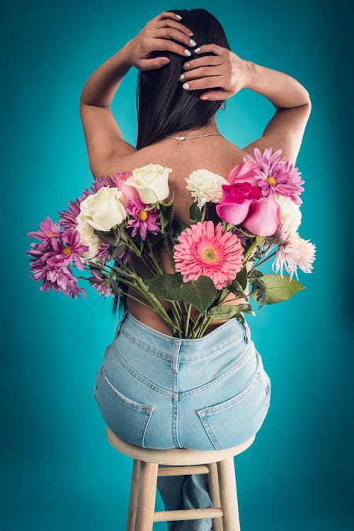 Back View of a Woman Sitting on a Chair with Flowers Tucked in the Back of Her Jeans 