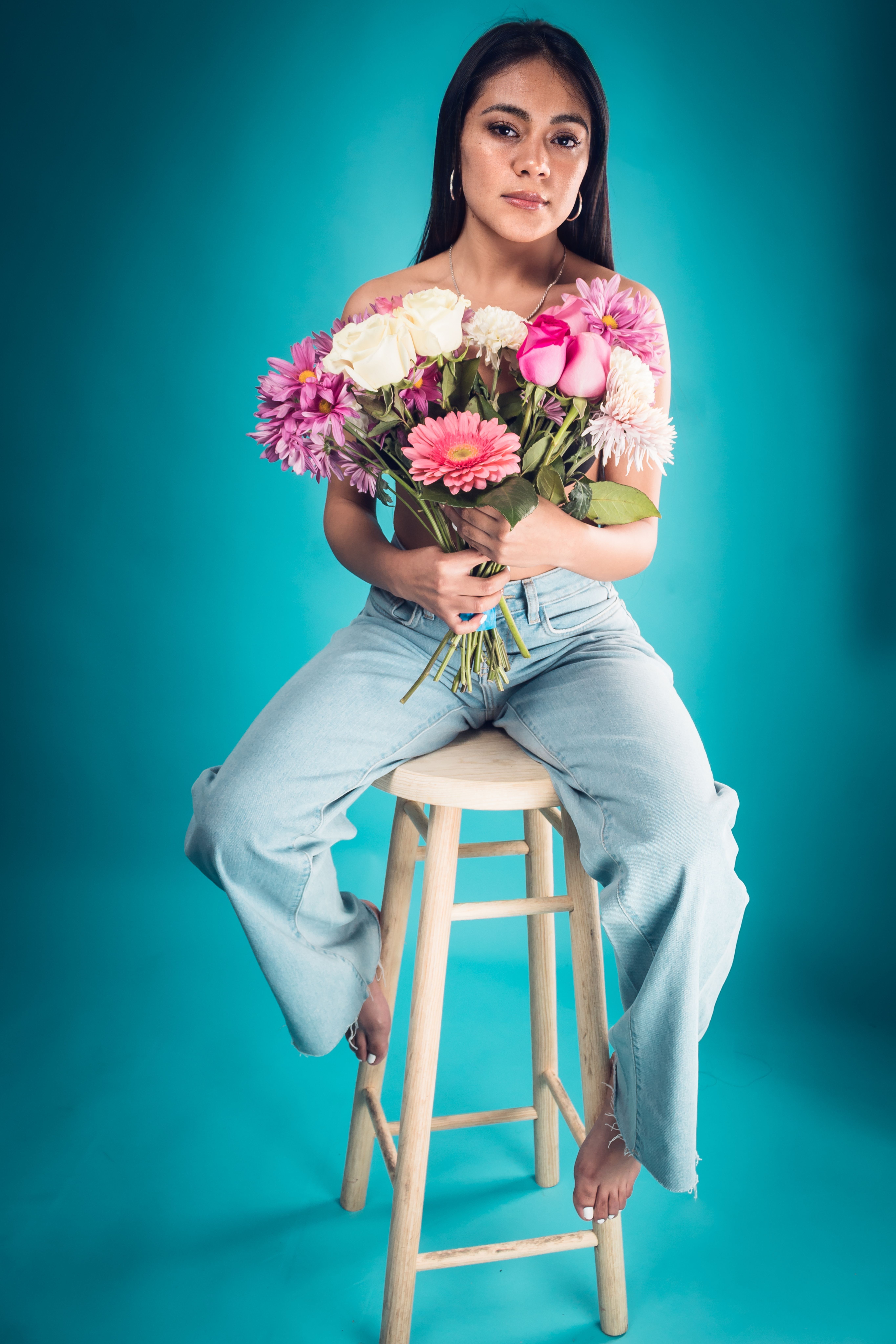 Young woman barefoot with a bouquet of flowers against blue studio background.