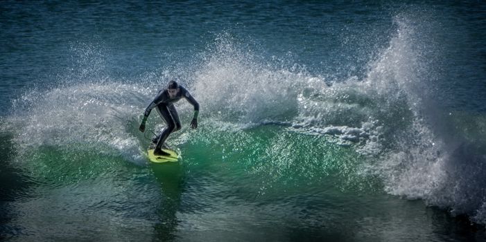 Surfer in wetsuit skillfully rides a wave, showcasing thrilling action and vibrant ocean scenery.
