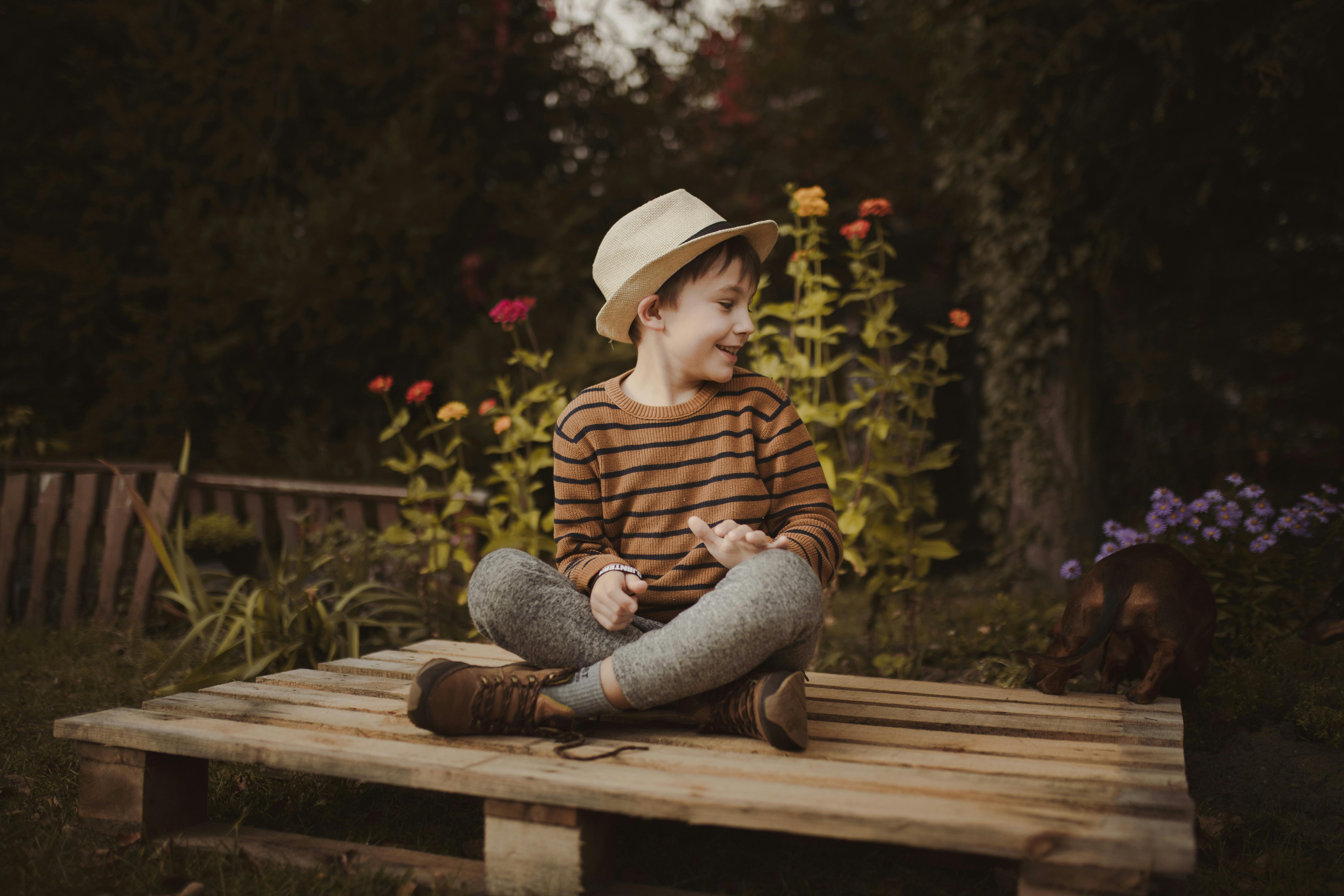 a young boy in brown striped sweater sitting on a wooden planks while looking over shoulder