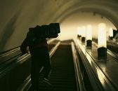 A man carrying items ascends an escalator in the Moscow Metro, captured in a low light setting.