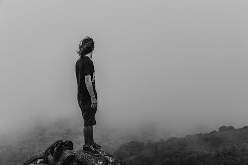 Grayscale Photo of a Man Standing on the Cliff 