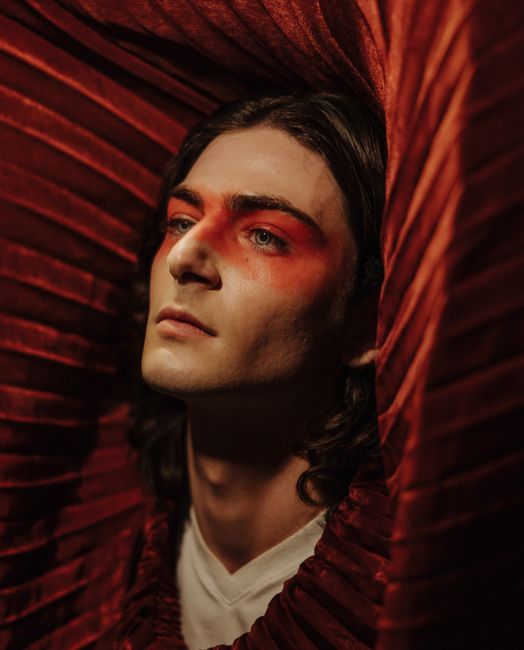 A striking artistic portrait of a person adorned with red makeup and surrounded by red fabric.