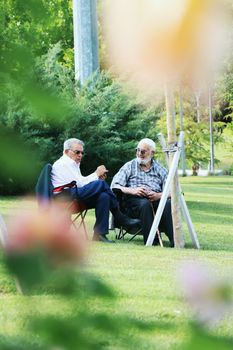Two senior men relaxing and chatting outdoors in a sunny park setting.