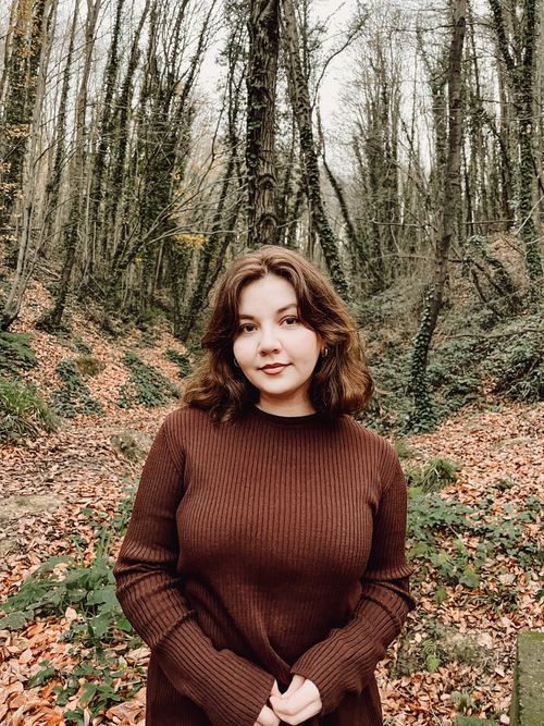 Free Woman in brown sweater standing in a serene autumn forest scene. Stock Photo