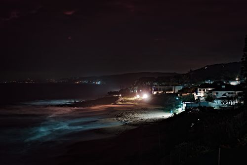 Free A peaceful night scene capturing the illuminated beach and coastal buildings, with waves gently lapping the shore. Stock Photo