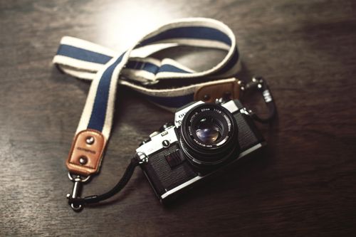Free A classic Olympus analog camera with a strap lies on a wooden table, showcasing vintage photography charm. Stock Photo