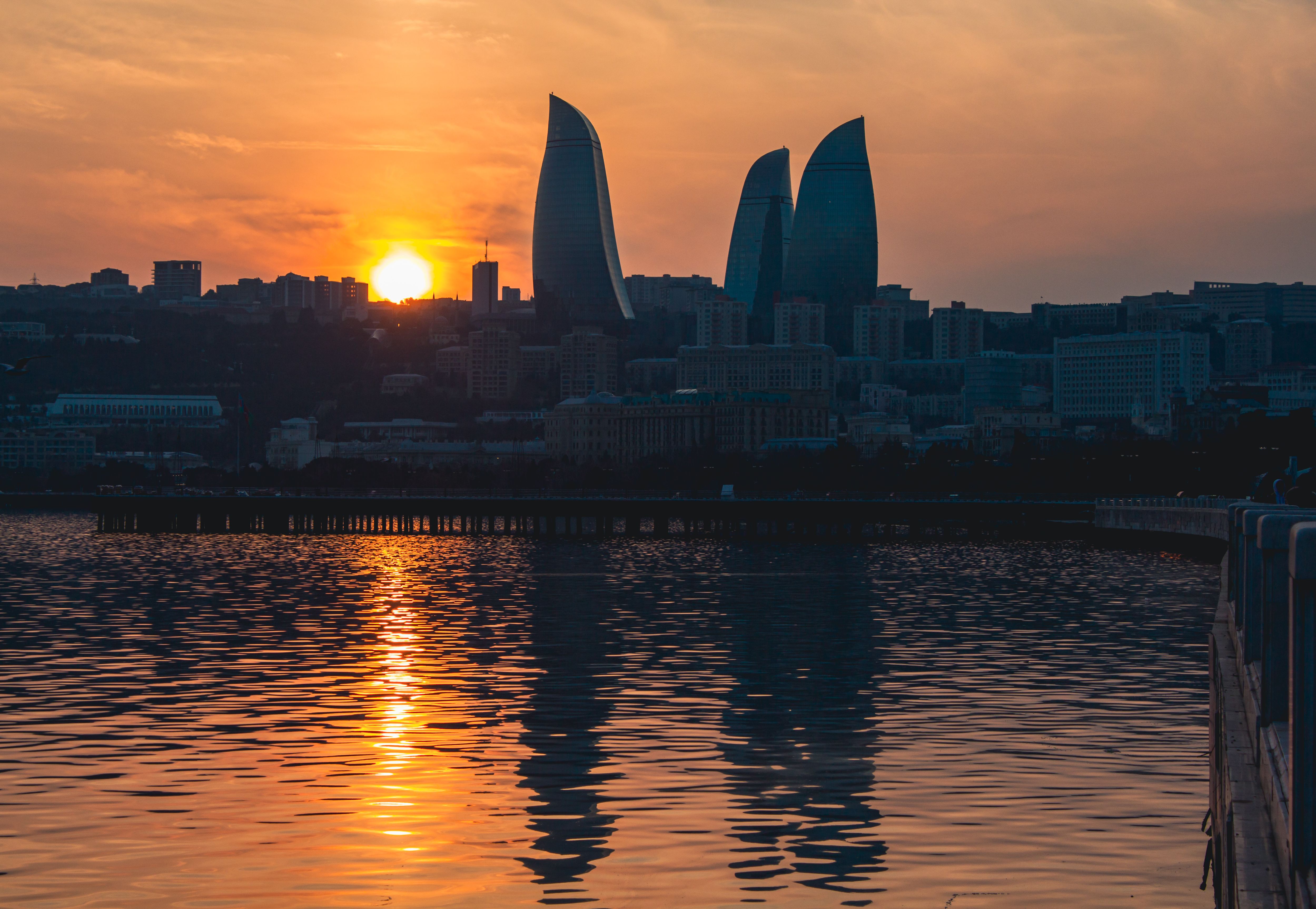 Silhouette of Baku's Flame Towers against a stunning sunset backdrop reflecting in the Caspian Sea.