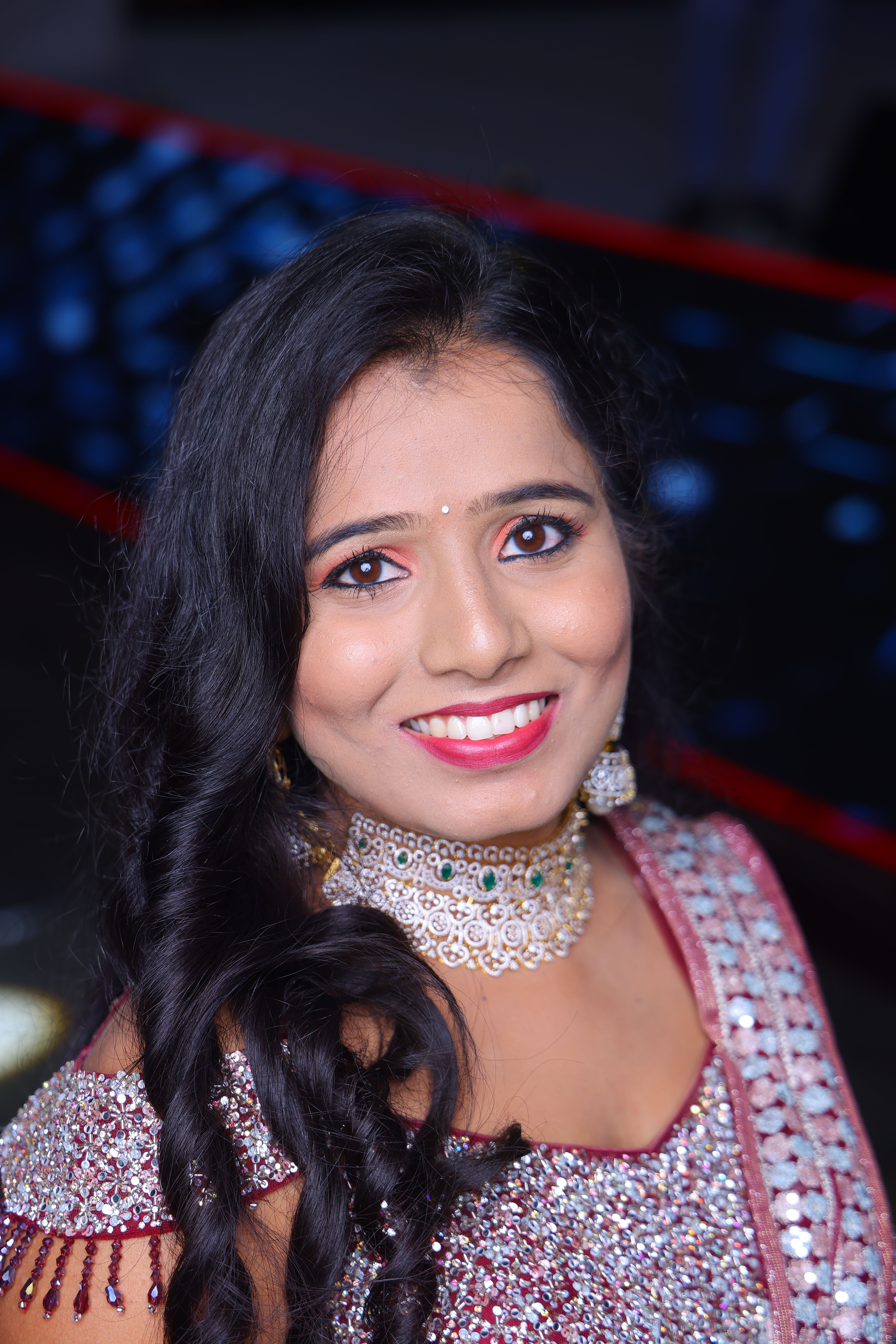 Portrait of an elegant Indian woman with intricate jewelry and traditional attire, smiling warmly.