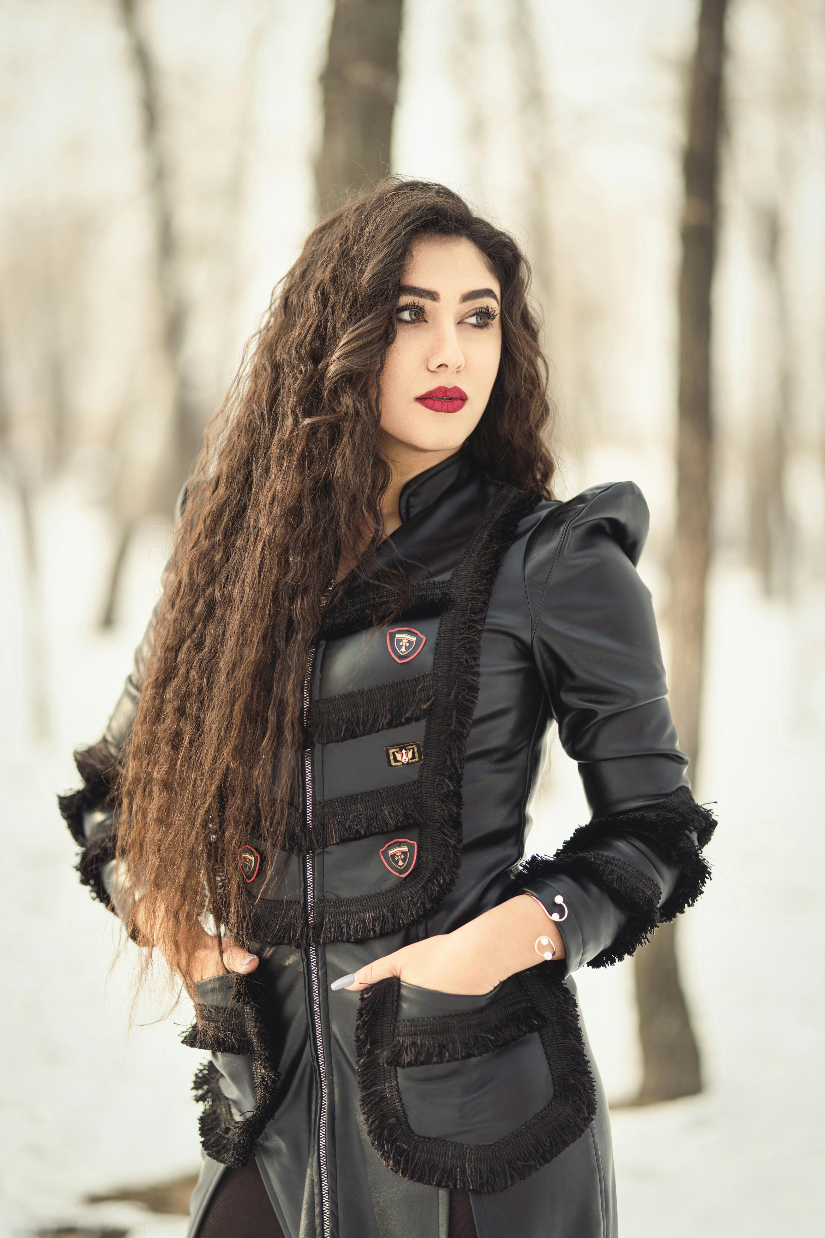 Elegant woman in leather dress poses in snowy forest setting during winter.