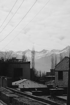 A black and white photo of mountain town buildings with fog and distant mountain range.