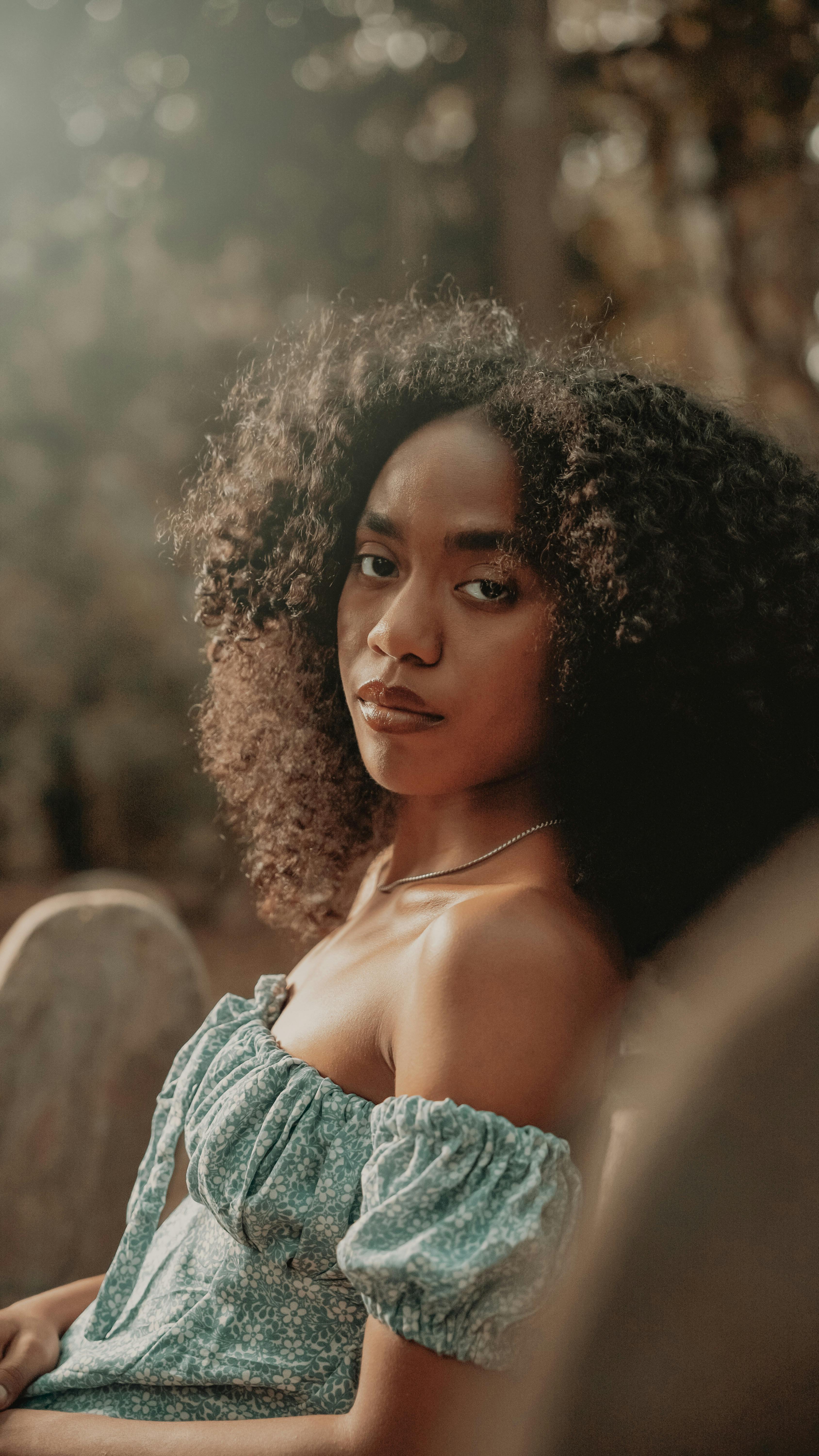 Portrait of a young woman with afro hairstyle sitting outdoors in summer light.