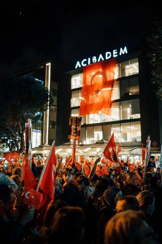 Gece ışıklı bir binanın önünde Türk bayraklarıyla toplanan kalabalık